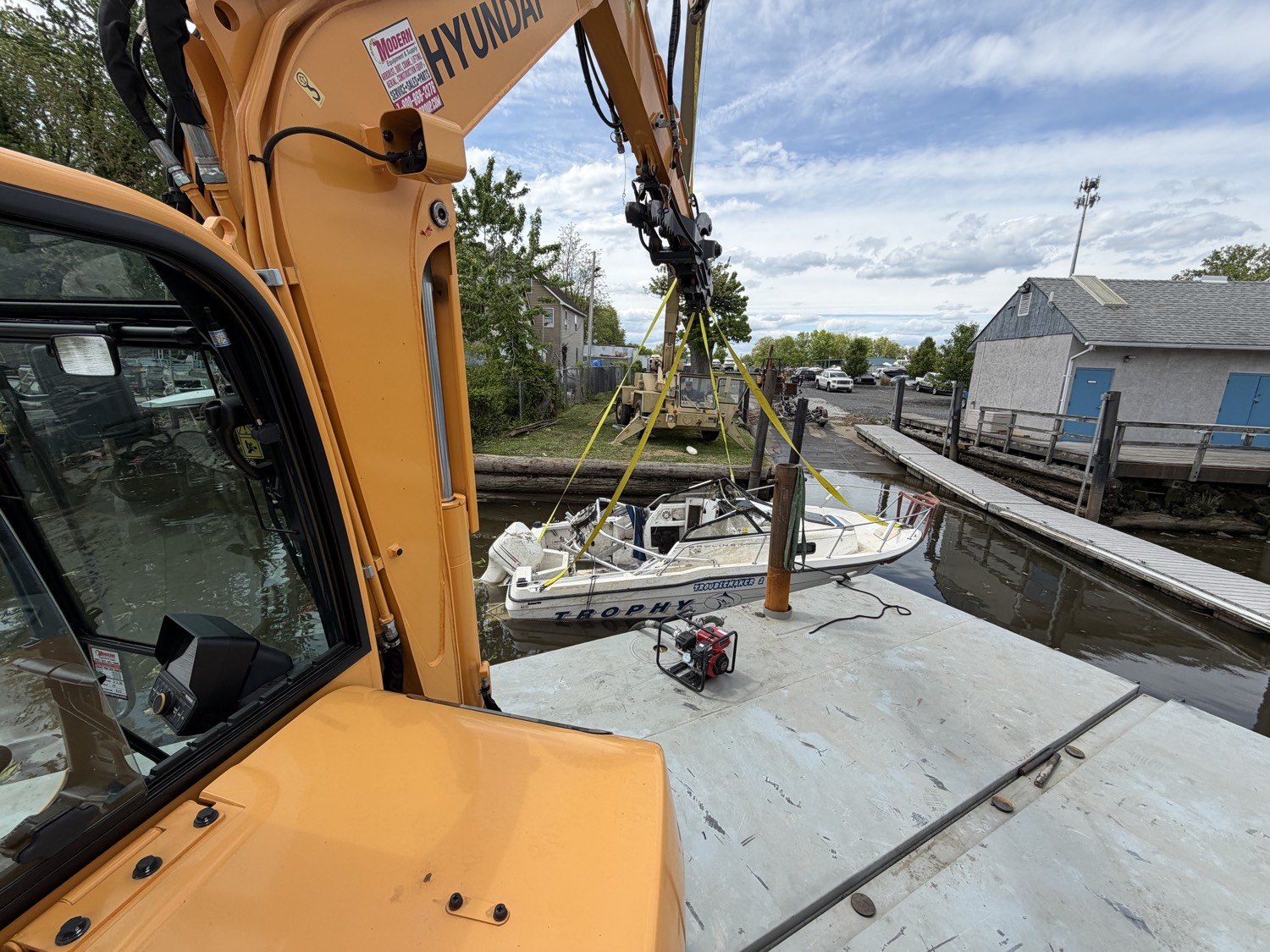 Sunken runabout being lifted from a canal with slings from the barge excavator